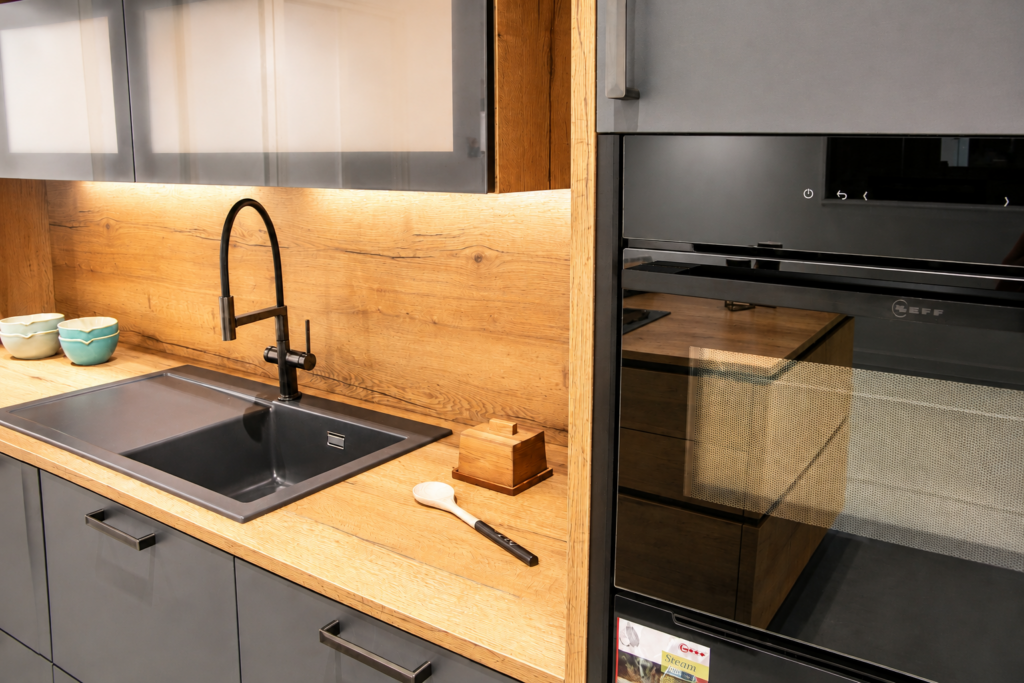 Moderner Spülbereich mit Holzoptik, dunkler Spüle und Einbau-Backofen in der Ausstellung des Küchencentrum Holtmann in Bückeburg