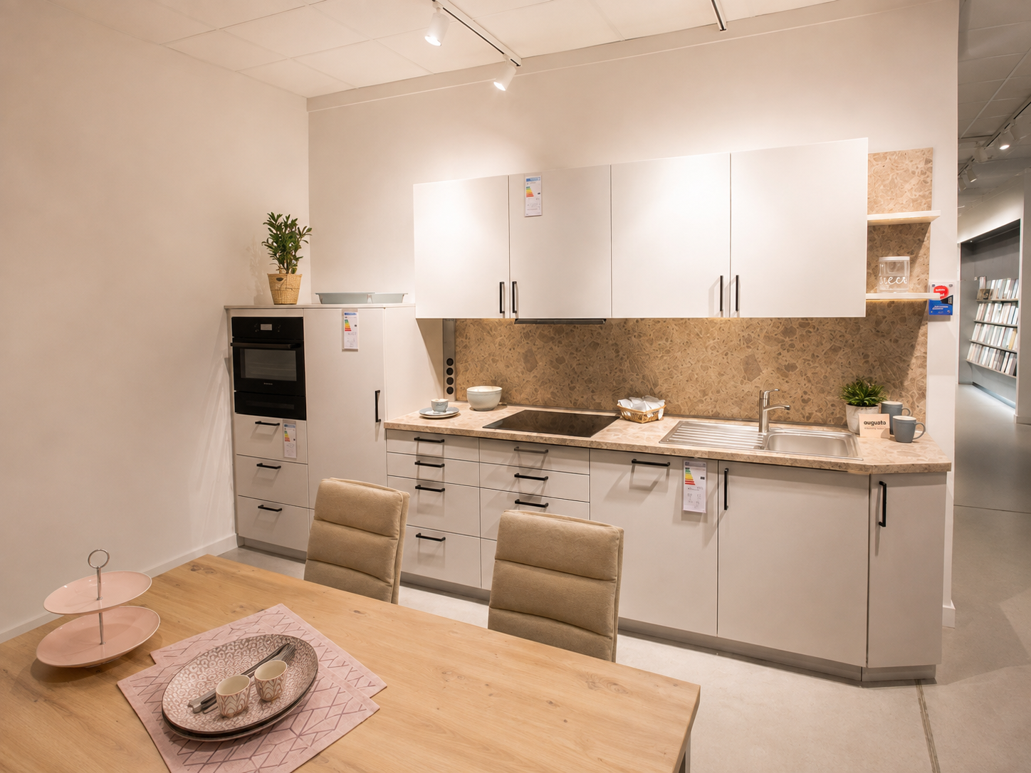 Weiße Ausstellungsküche mit Essbereich, schwarzem Induktionskochfeld und Arbeitsplatte in Steinoptik im Küchencentrum Holtmann in Bückeburg